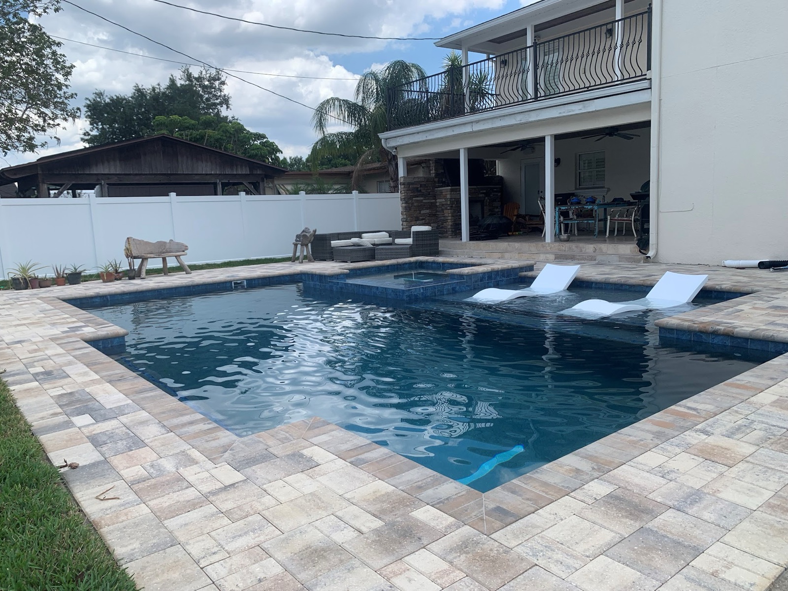 Pool with raised spa, in-water loungers, and paver deck behind a two-story home