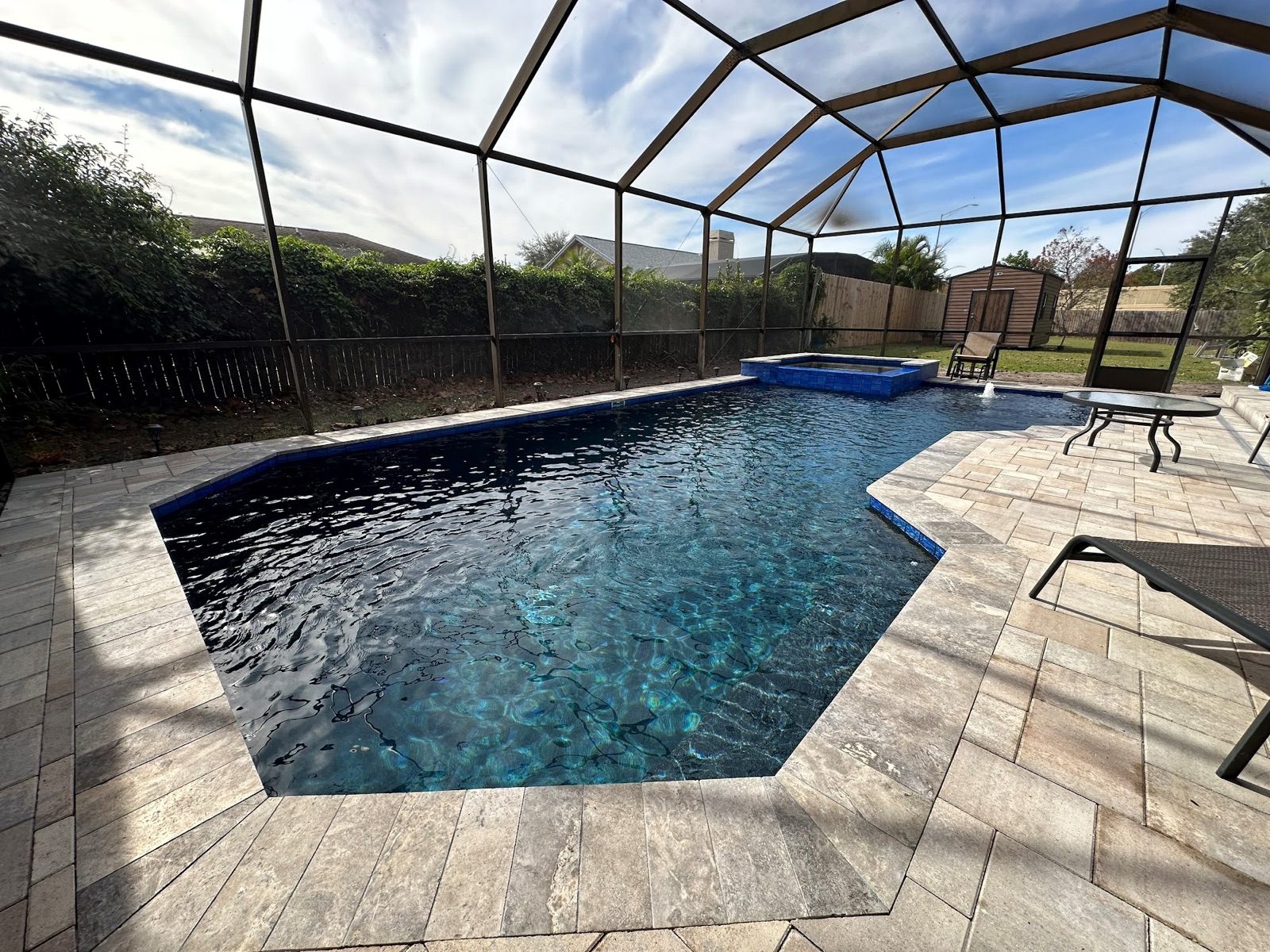 Resurfaced pool inside screen enclosure with travertine deck
